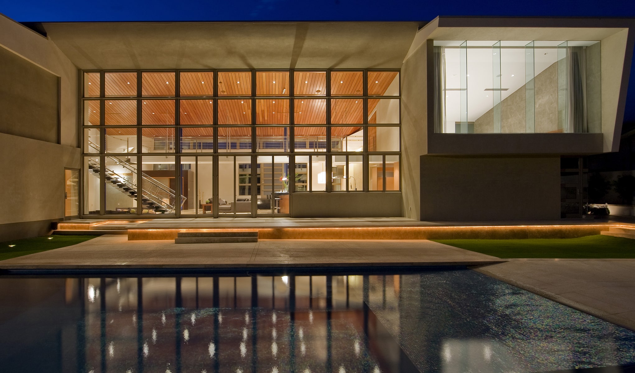 A contemporary house with a pool illuminated at night, showcasing its modern design and inviting ambiance.